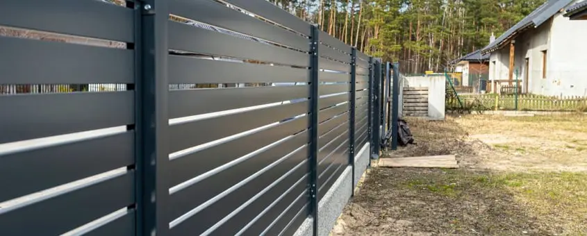 Reja de herrería con perfiles acomodados en posición horizontal protegiendo un jardín