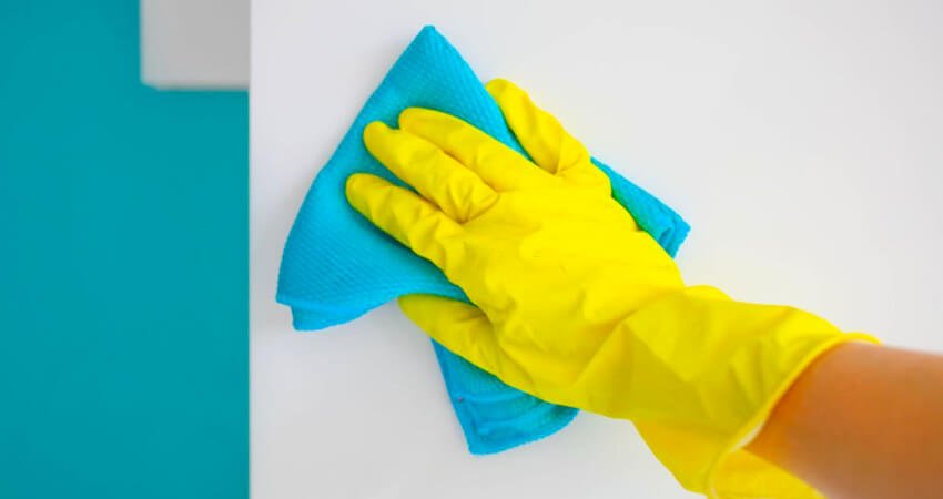 Mano con guante amarillo limpiando pared con paño