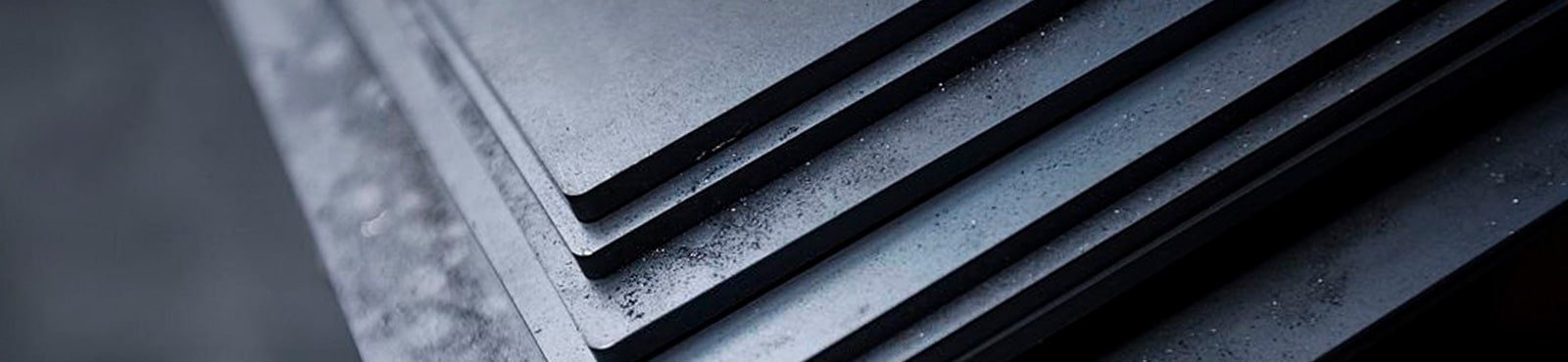 Placas de acero de diversos calibres y medidas aseguradas con una cinta apiladas dentro de una fábrica