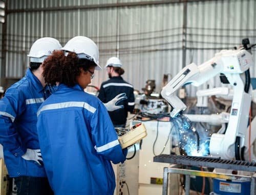 Ingenieros supervisando el trabajo de un robot que manipula y corta piezas de acero